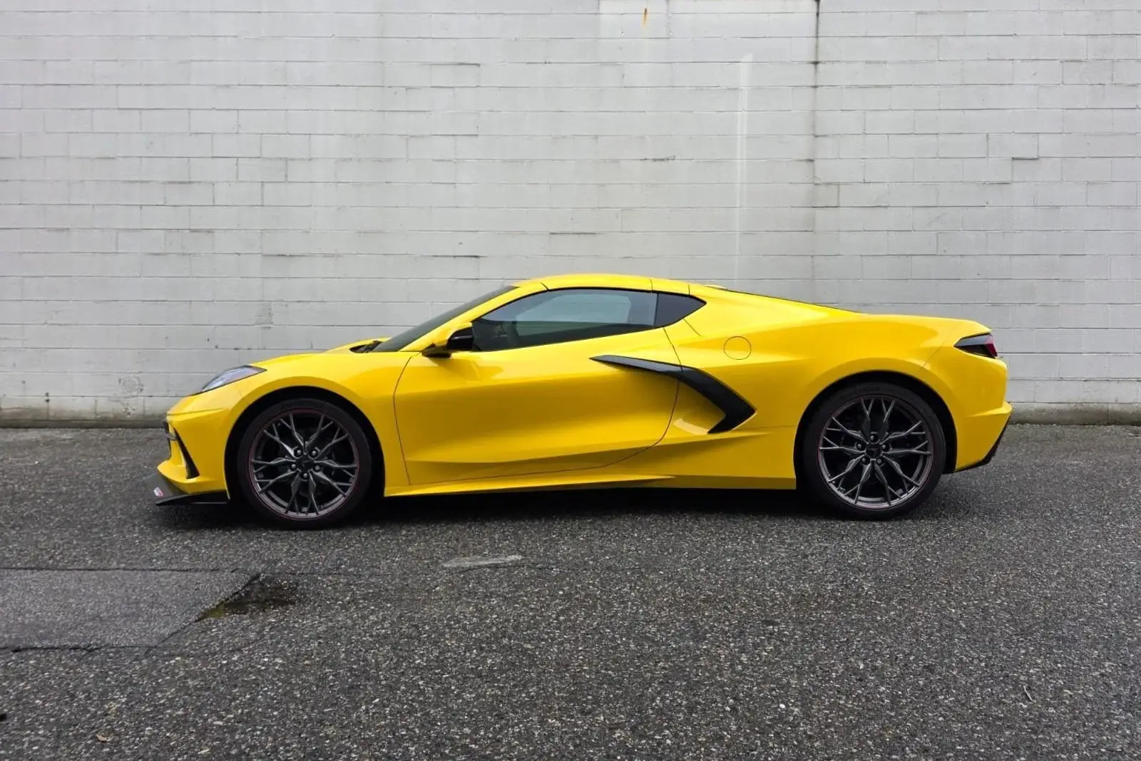 Side profile of a yellow Corvette C8 against a white block wall
