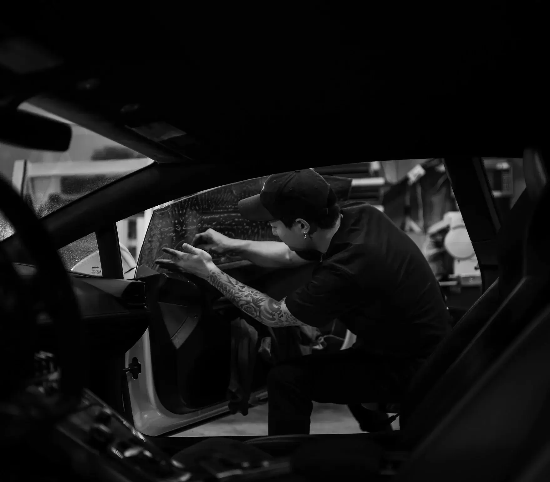 Technician working on a rear door window from inside the car, black and white