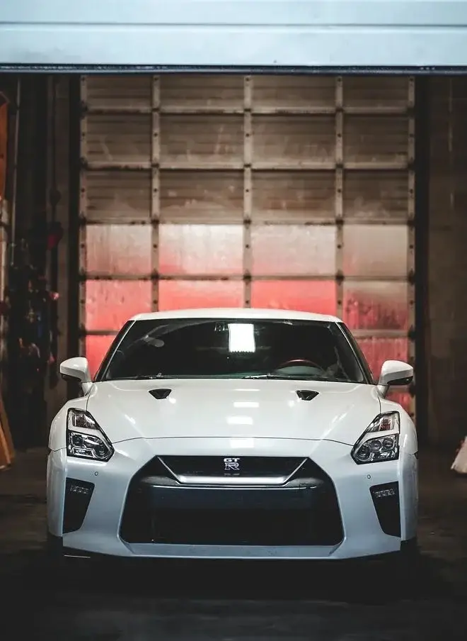 White Nissan GT-R facing the camera in a red-lit shop bay