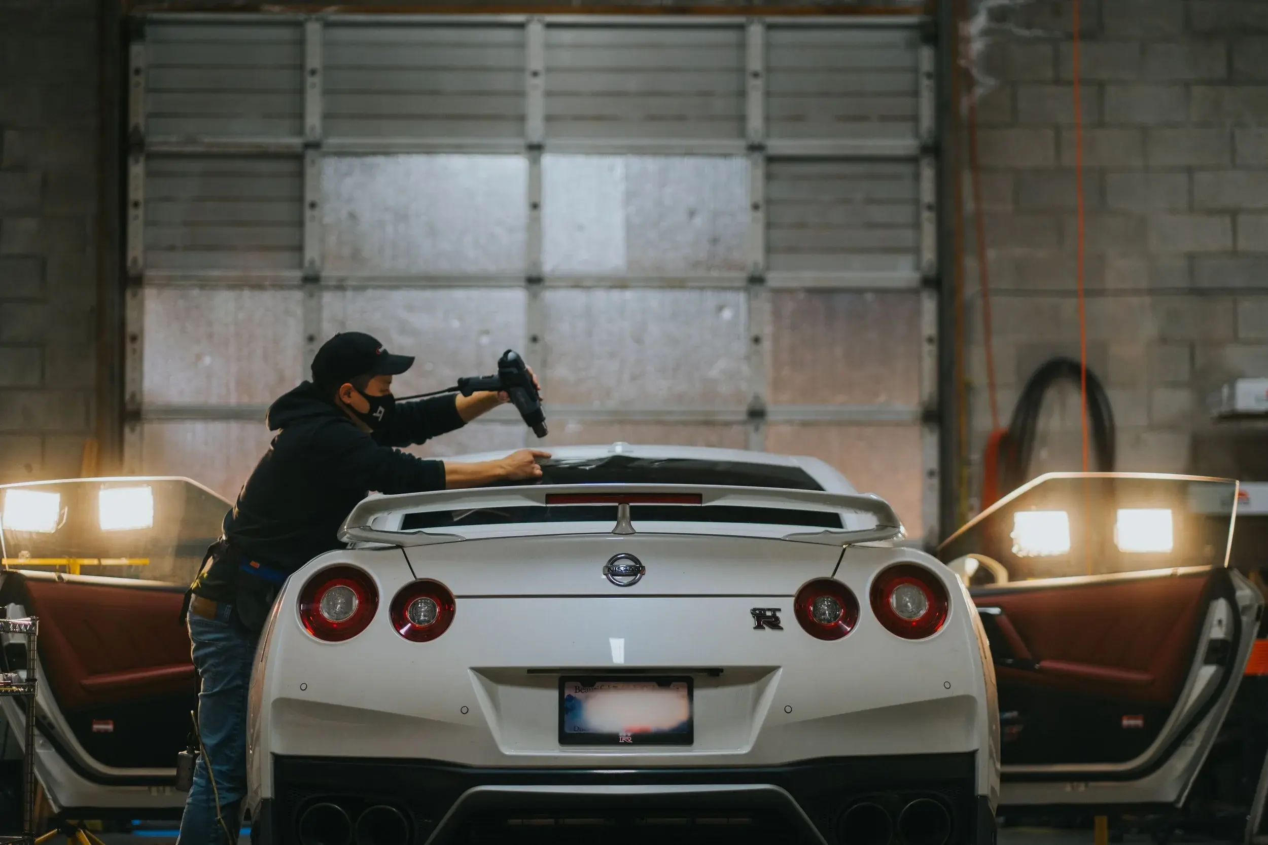 Technician heat-shrinking window film on the rear glass of a white Nissan GT-R inside Brookswood Tint Shop