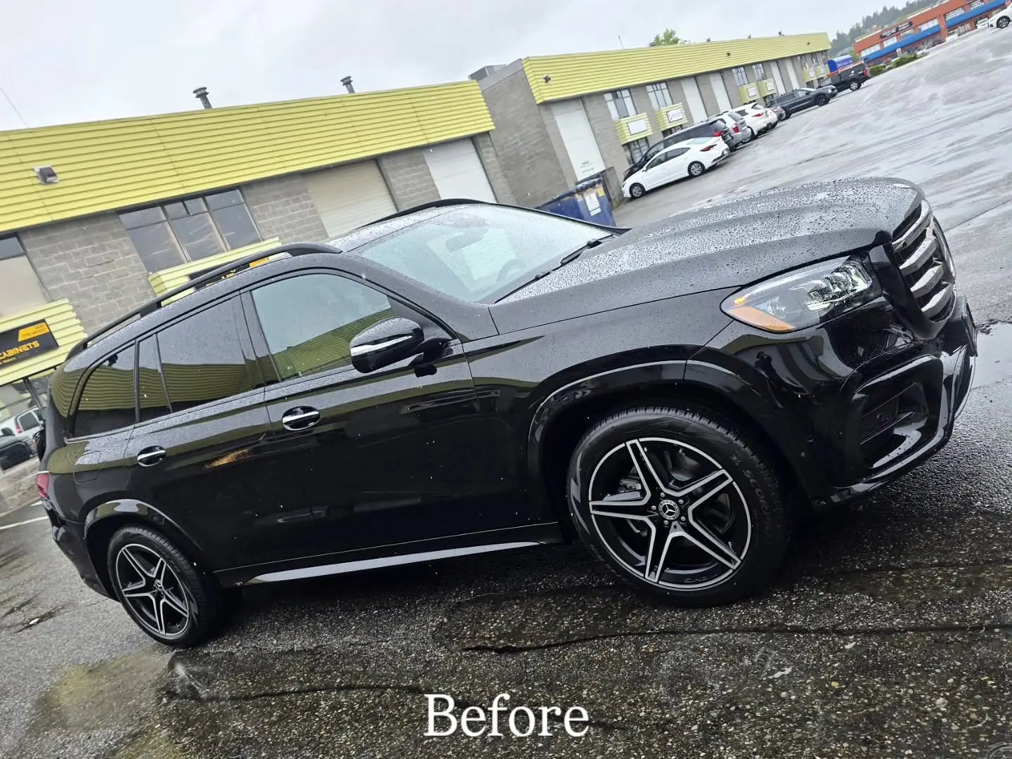 The same Mercedes GLS in gloss black paint, wet with rain in the parking lot before the wrap