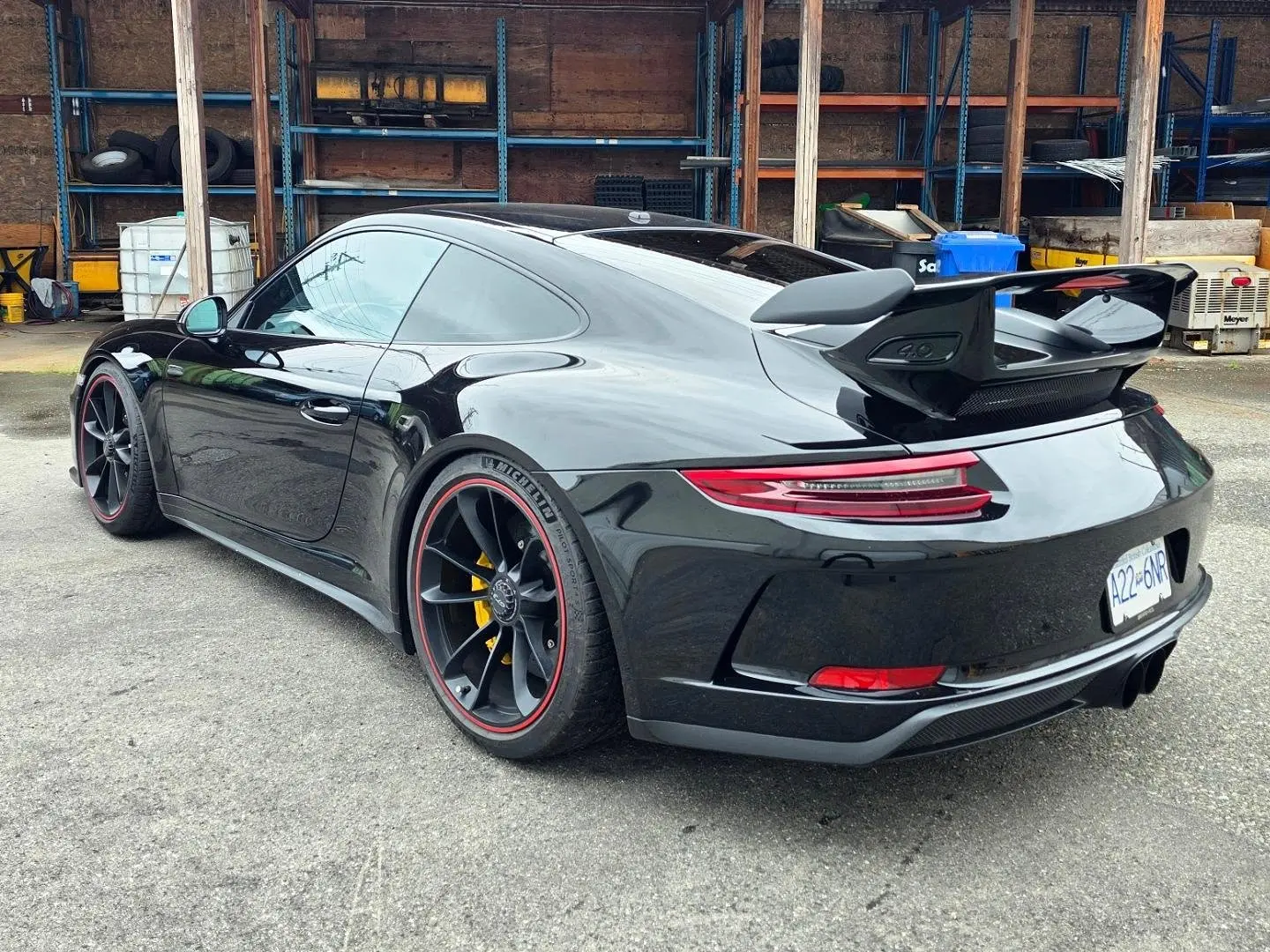 The same black 911 GT3 from the rear three-quarter in a yard lined with tire racks, its rear quarter window and back glass carrying ceramic film