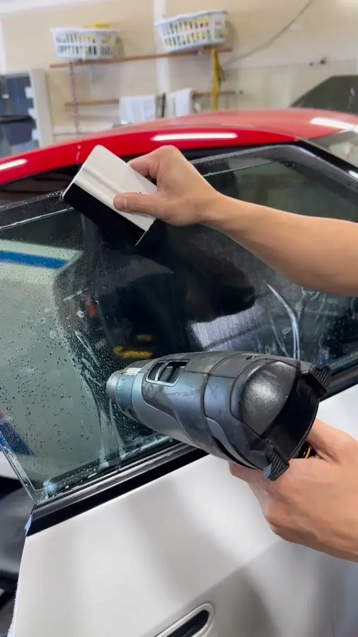 Brookswood Tint technician in Langley shrinking window film onto a side window with a heat gun, a hard card in the other hand