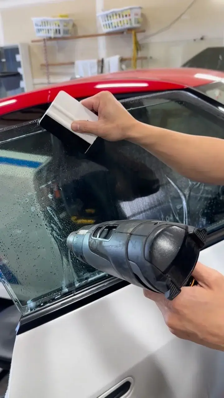 Technician heat-forming film on a red car's rear quarter window