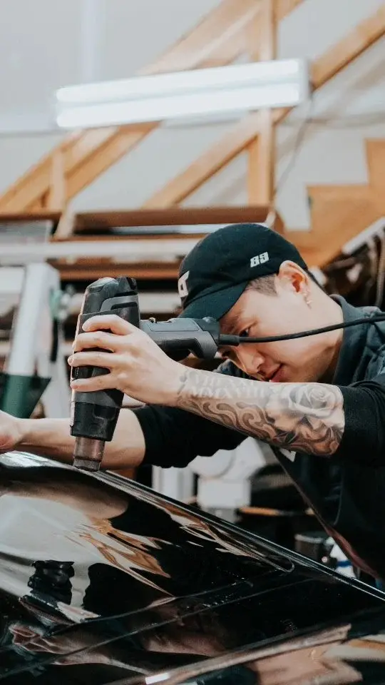 Technician working a heat gun over a glossy black car inside the Brookswood Tint shop in Langley