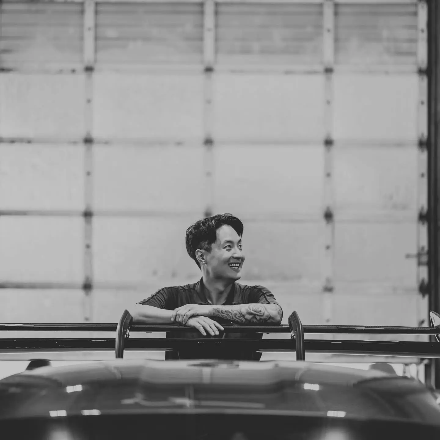 Johnny, owner of Brookswood Tint Shop, leaning on a car in the bay, black and white