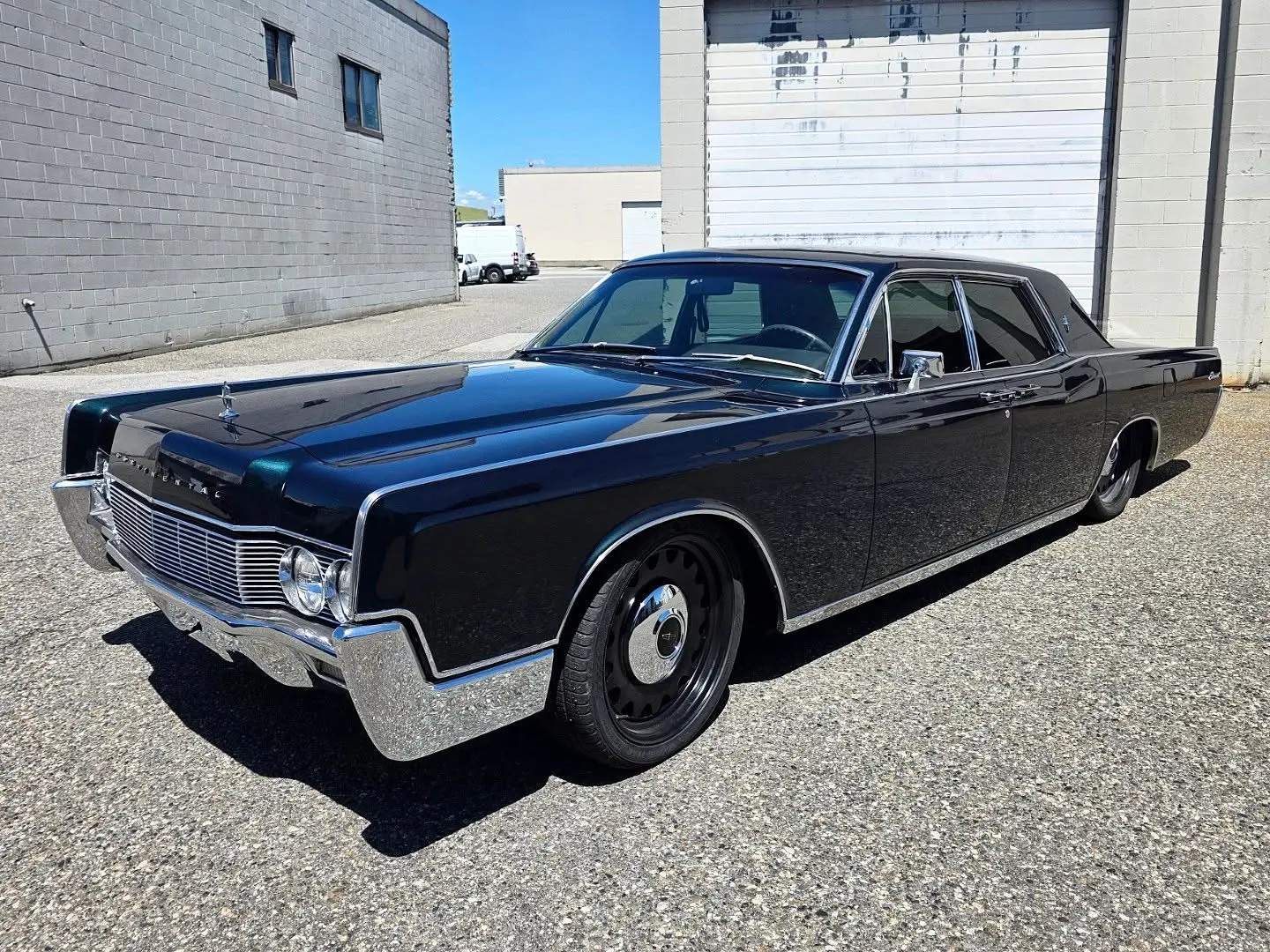 Driver's side of the 1967 Continental, a chrome mirror on the front door and darker glass in the rear door, parked by a roll-up bay door