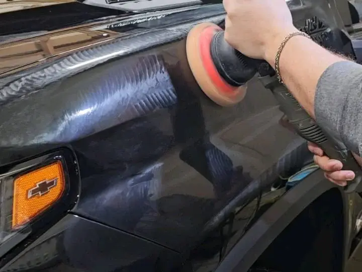 Orbital polisher correcting paint on a black Chevrolet fender