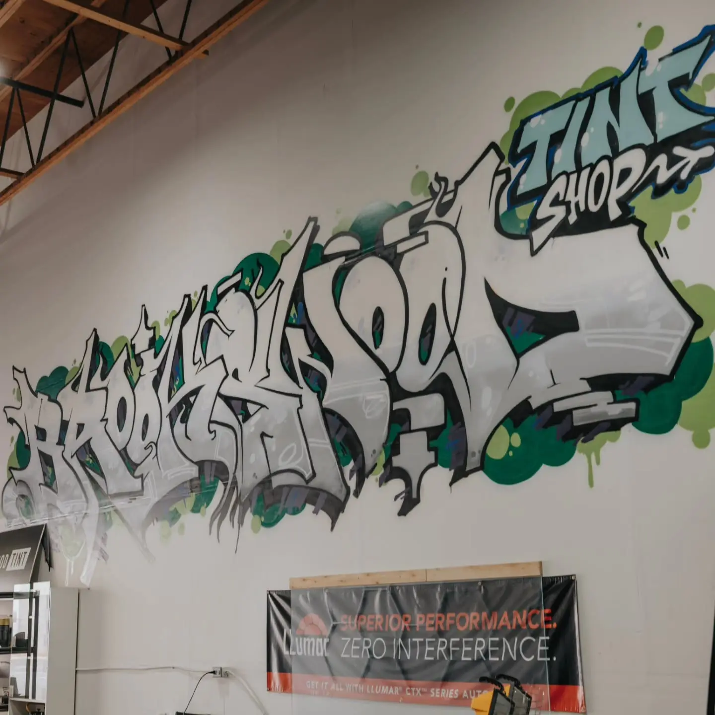 Graffiti mural spelling out Brookswood Tint Shop on the shop's interior wall, above a LLumar banner reading Superior Performance, Zero Interference, which promotes the CTX series