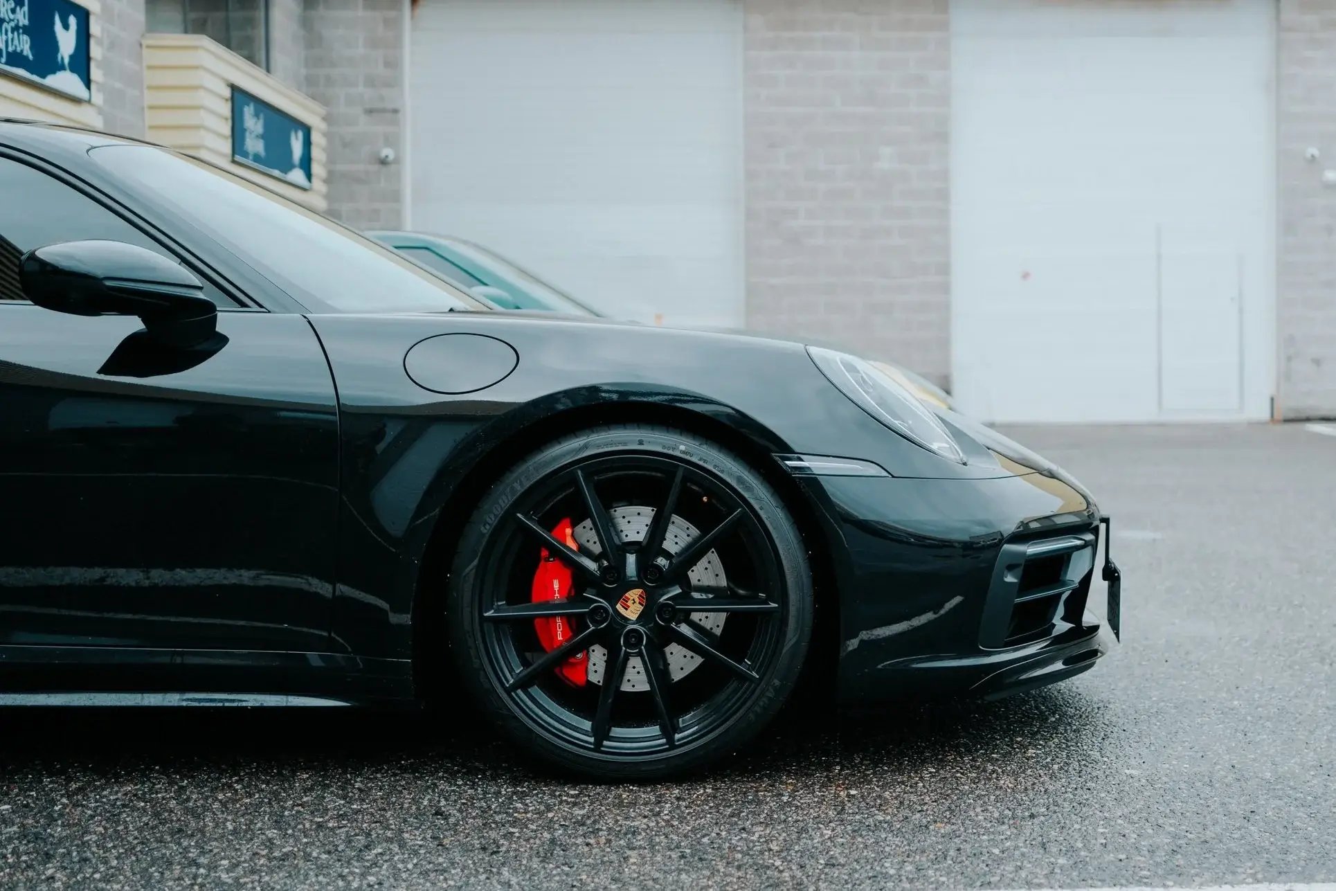 Black Porsche 911 with red brake calipers parked on wet asphalt