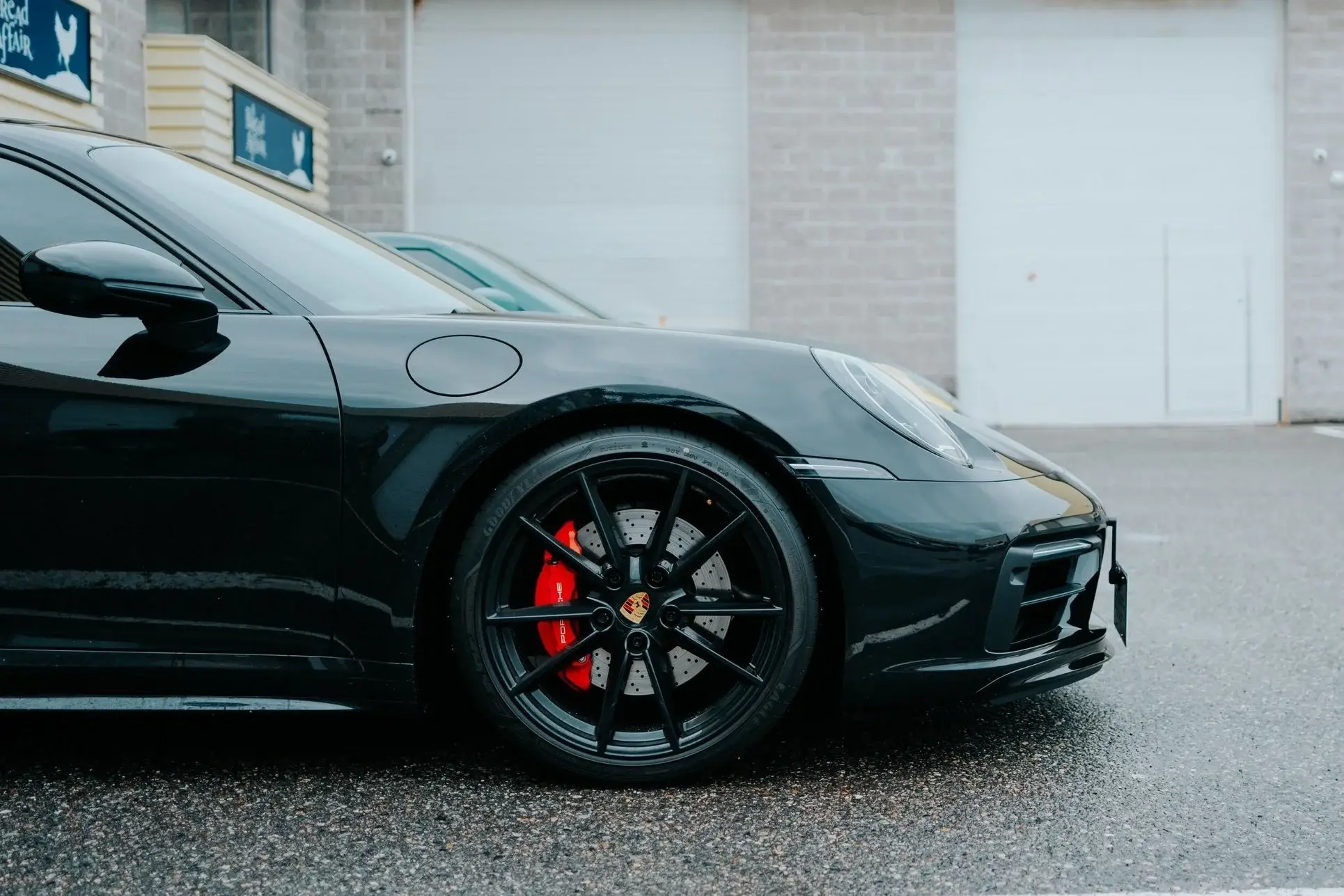 Black Porsche 911 with red brake calipers on wet asphalt, water beading on the paint