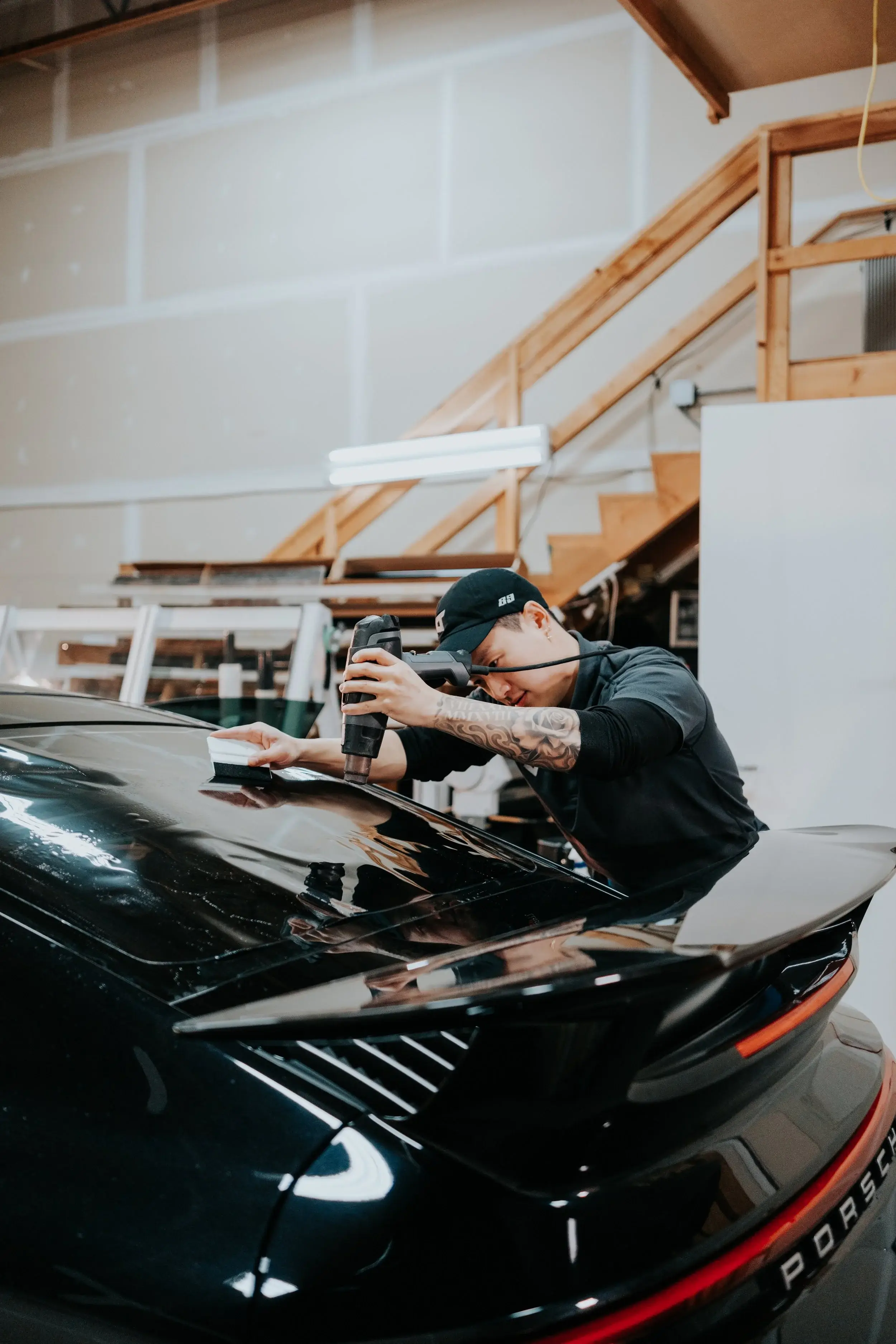 Technician squeegeeing film onto the rear deck of a black Porsche 911