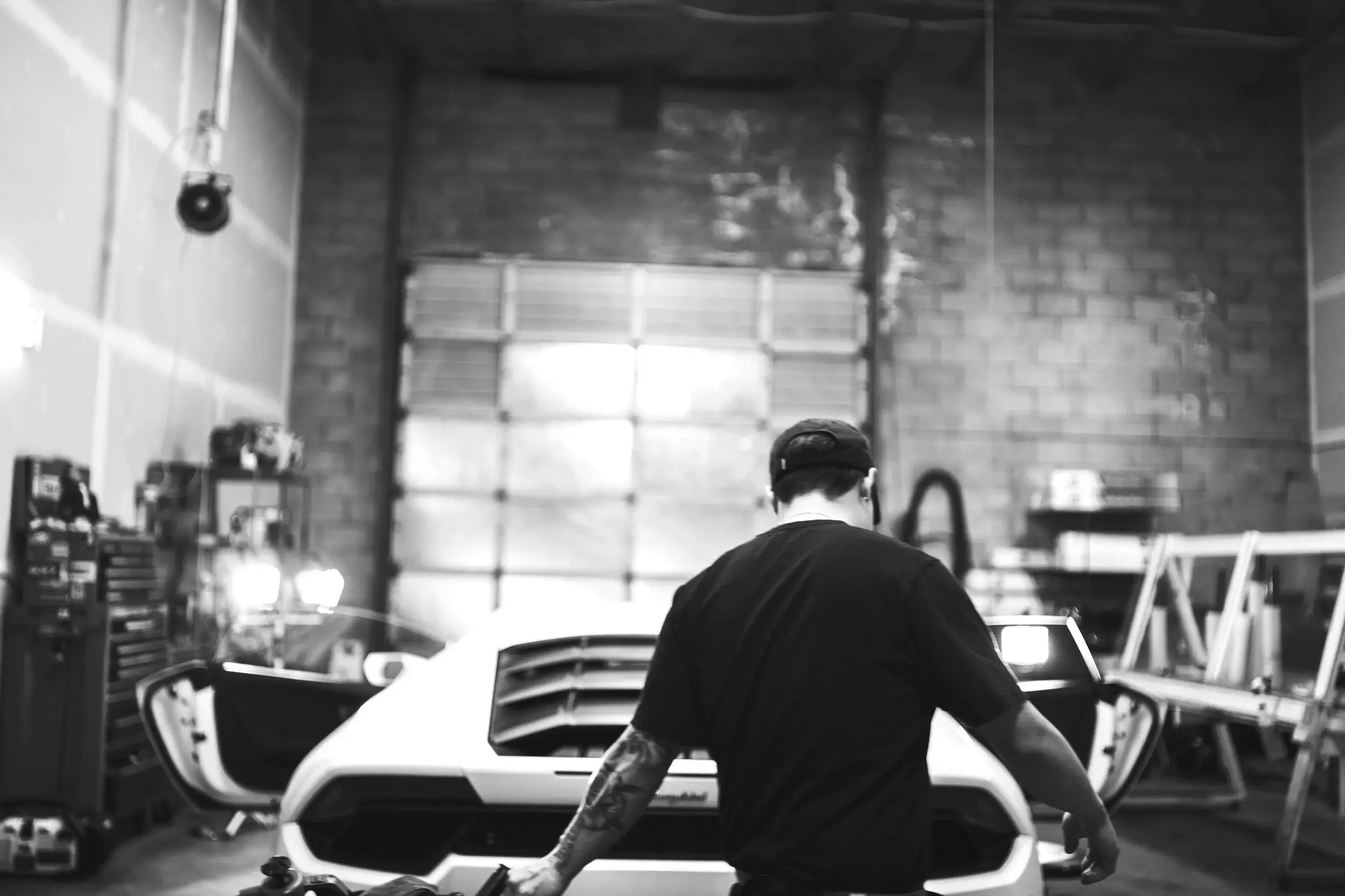 Black and white view of a technician working beside a white sports car in the shop