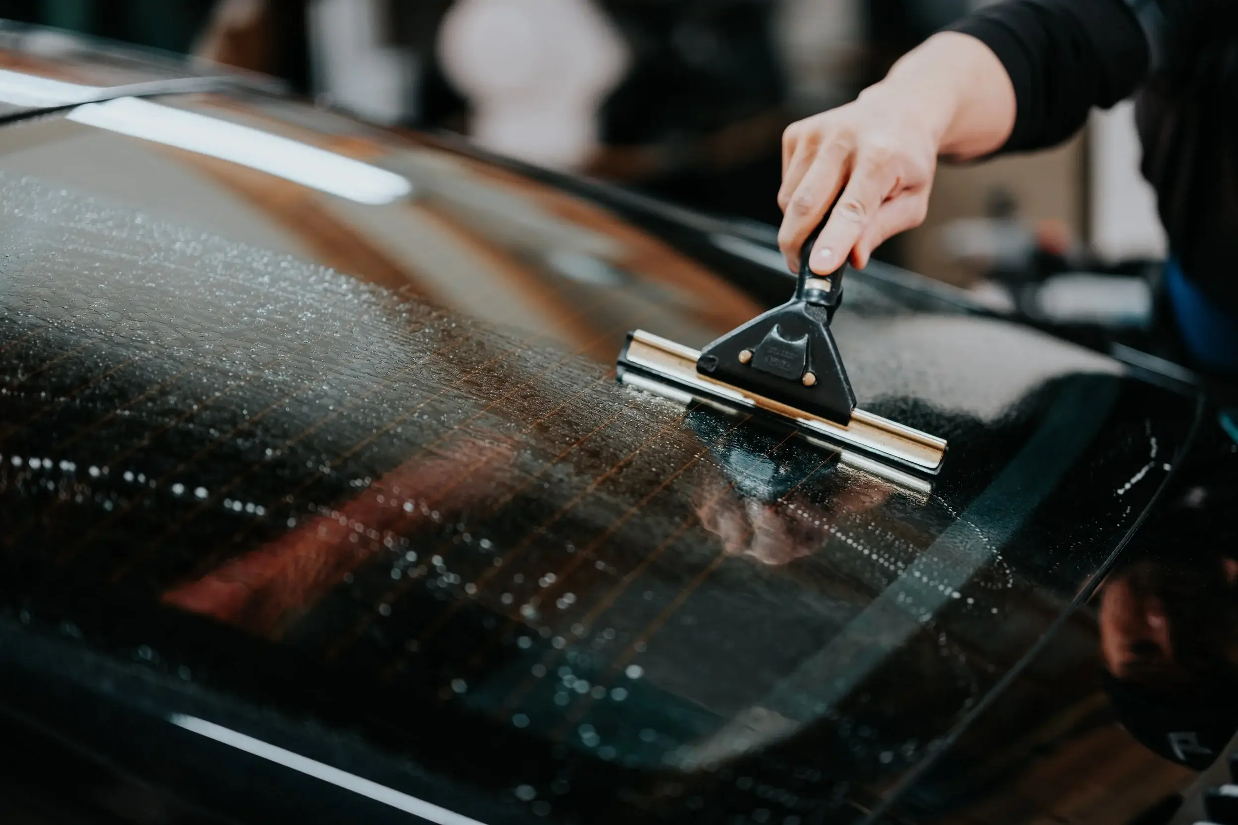 Squeegee pressing window film onto tinted glass, water beading on the surface