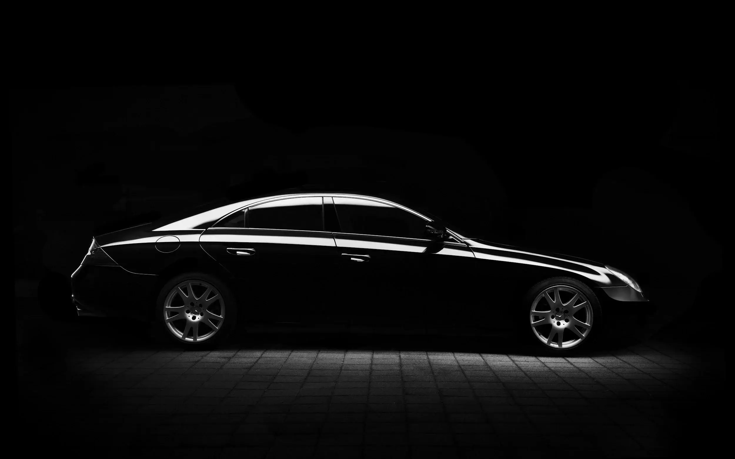 Black Mercedes CLS sedan with dark side glass, shown in profile against a black background