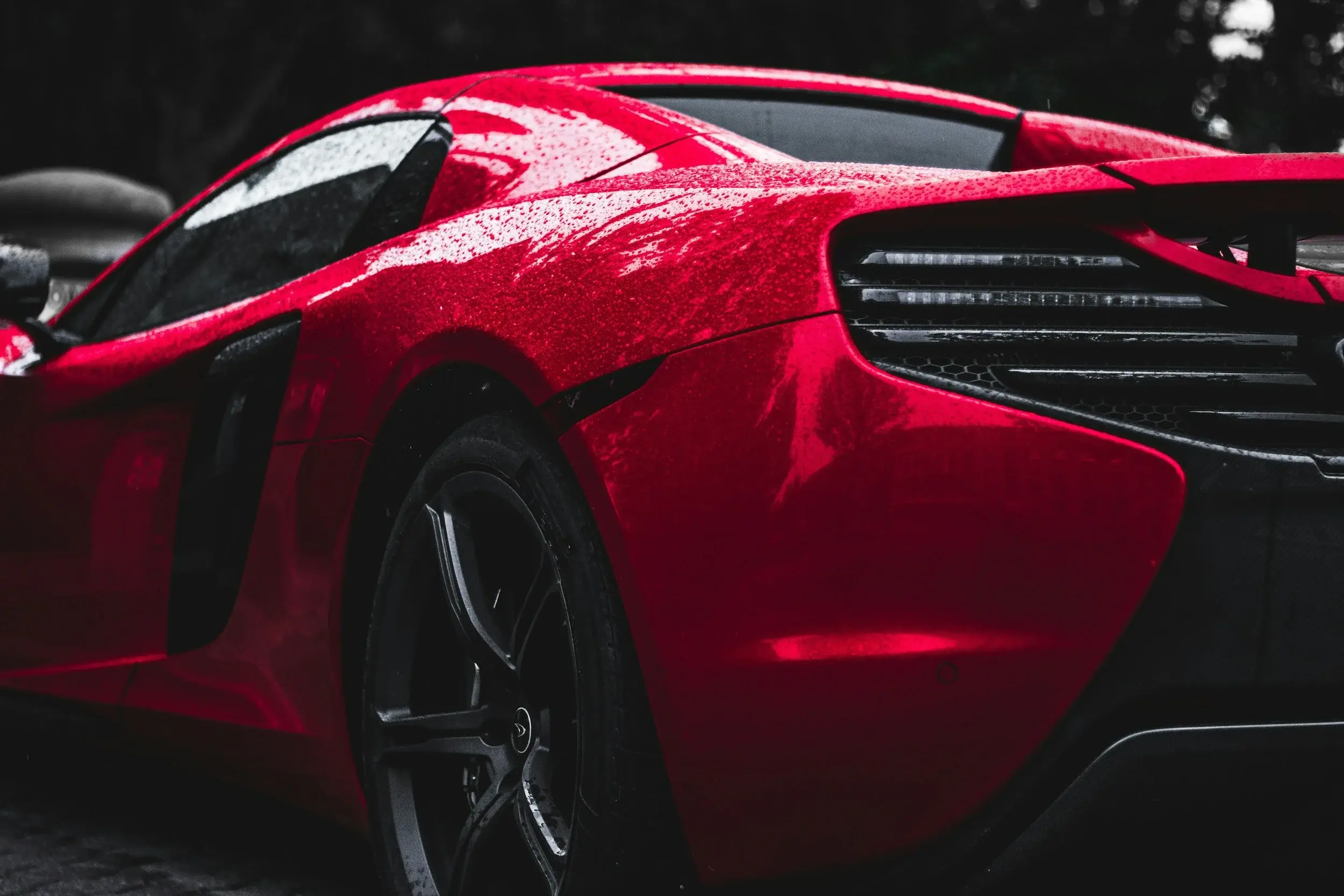 Raindrops beading on the red rear fender and side intake of a McLaren sports car