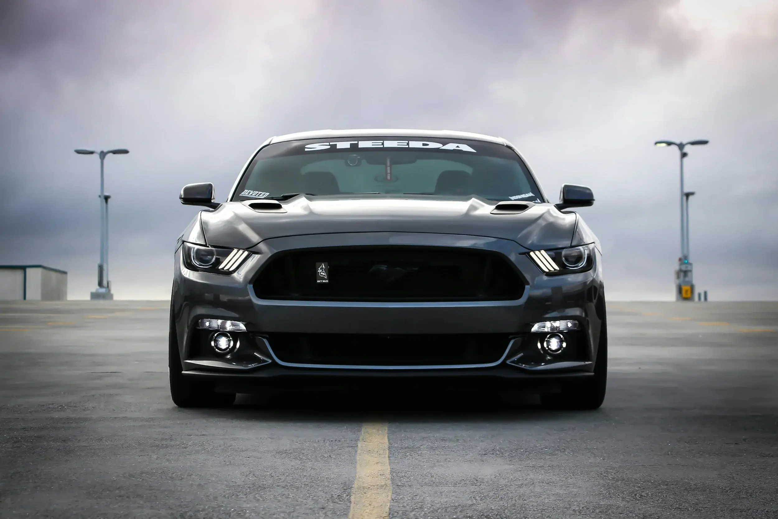 Stock photo of a dark grey Ford Mustang GT from the front, its three-bar LED running lights glowing in each headlamp