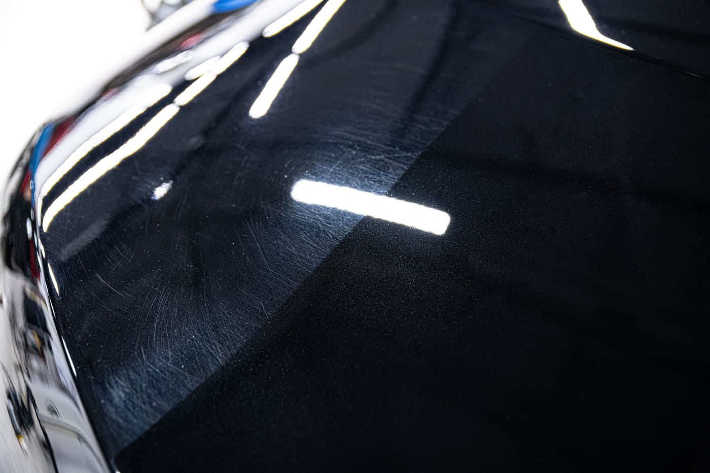 Black car paint with fine swirl marks on one half and a clear, mirror-like corrected finish on the other