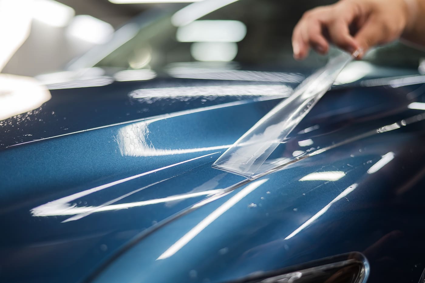 Installer laying a sheet of clear paint protection film onto the hood of a blue car