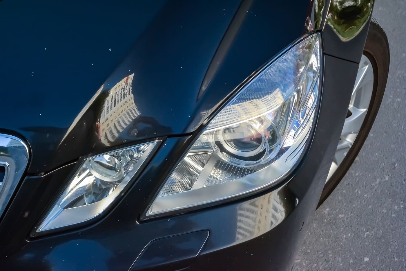 Front of a black car with small white stone chips scattered along the leading edge of the hood and the fender