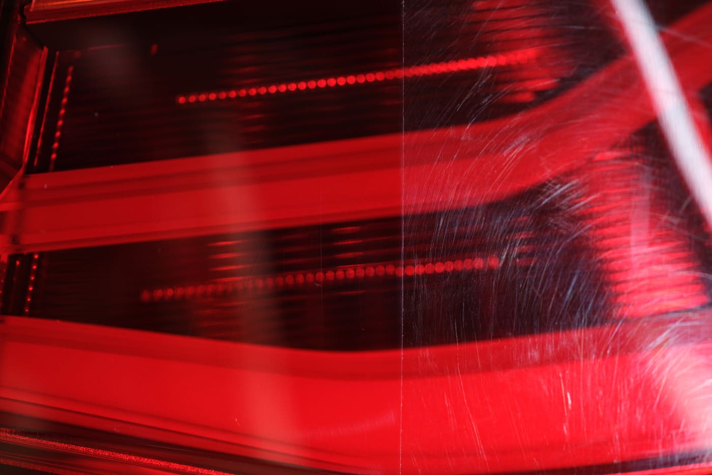 Red car taillight lens, polished clear on the left half and scratched and hazy on the right half