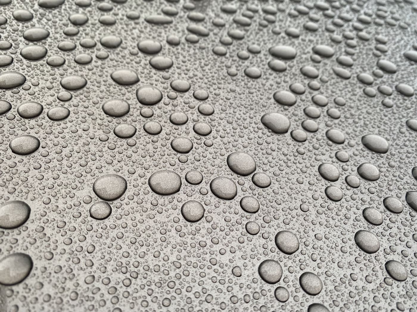 Water beading into tight round droplets on grey car paint